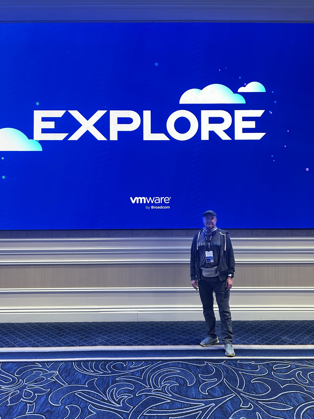 Robert Greenlee standing alone in front of a large illuminated VMware Explore screen in an empty ballroom