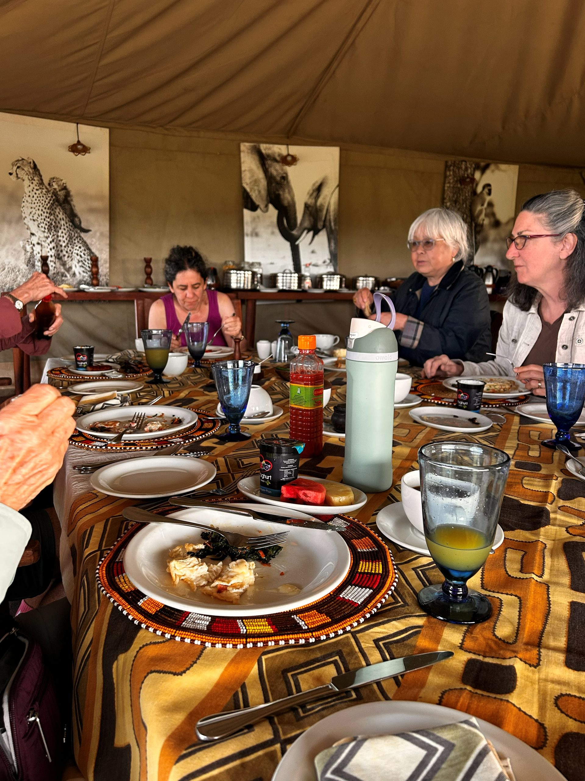 Group at breakfast in the Nyumba dining tent — beaded Maasai placemats, blue glassware, wildlife art on canvas walls