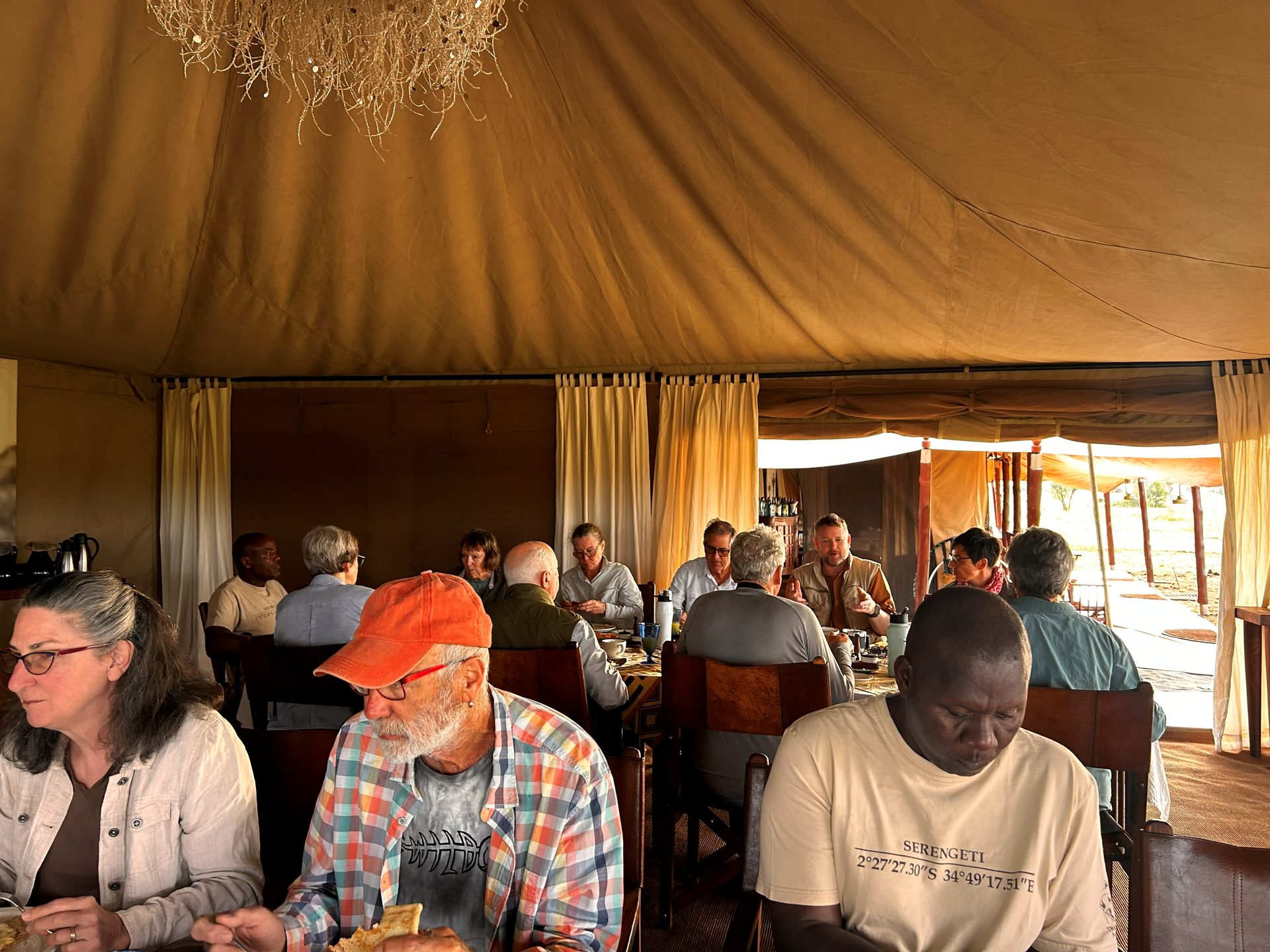The full group eating breakfast inside the Serengeti Nyumba camp dining tent — warm canvas light, everyone gathered at the long table