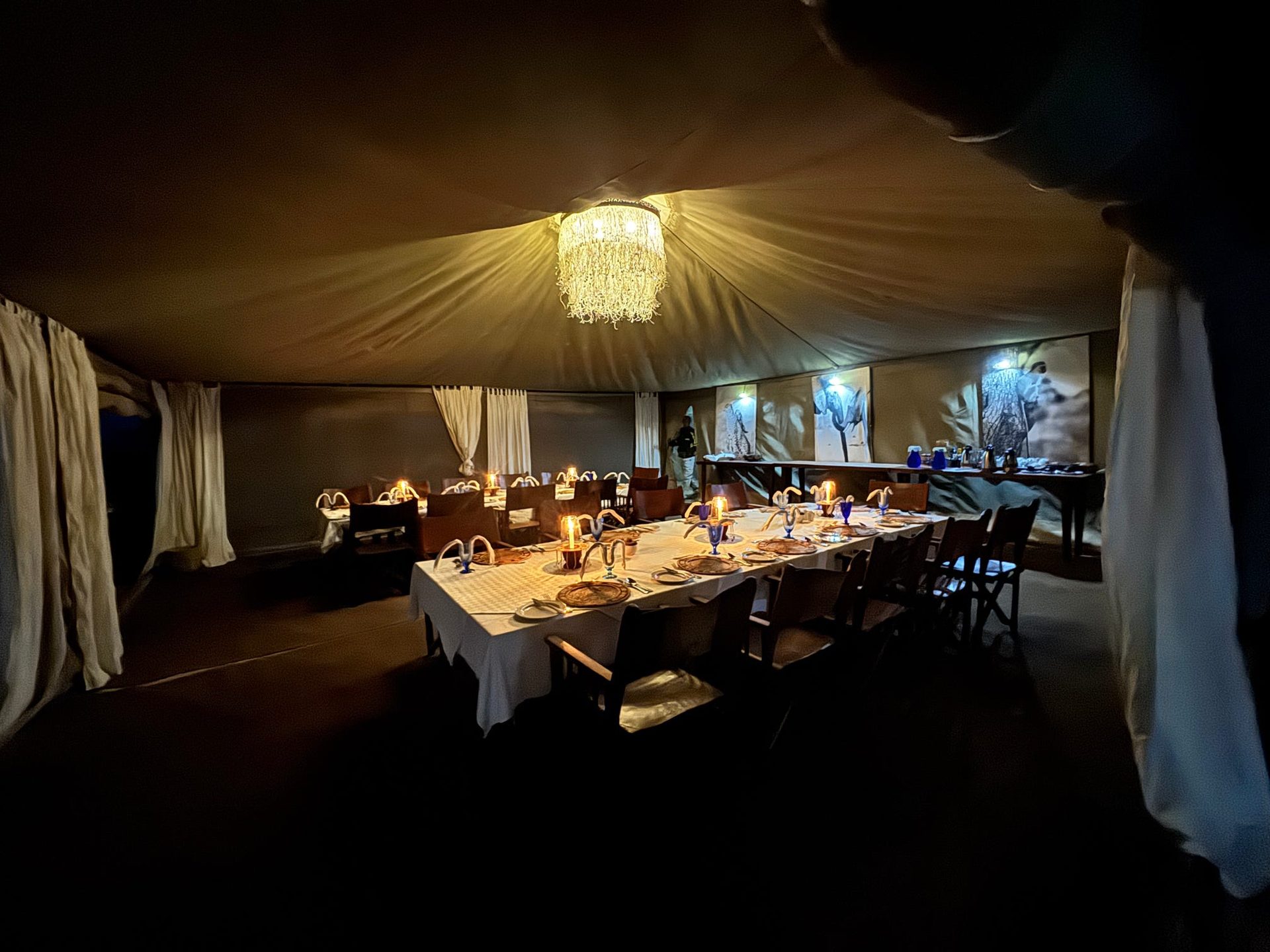 Candlelit dinner inside the Tarangire Safari Lodge dining tent — beaded chandelier, white linen, blue glassware