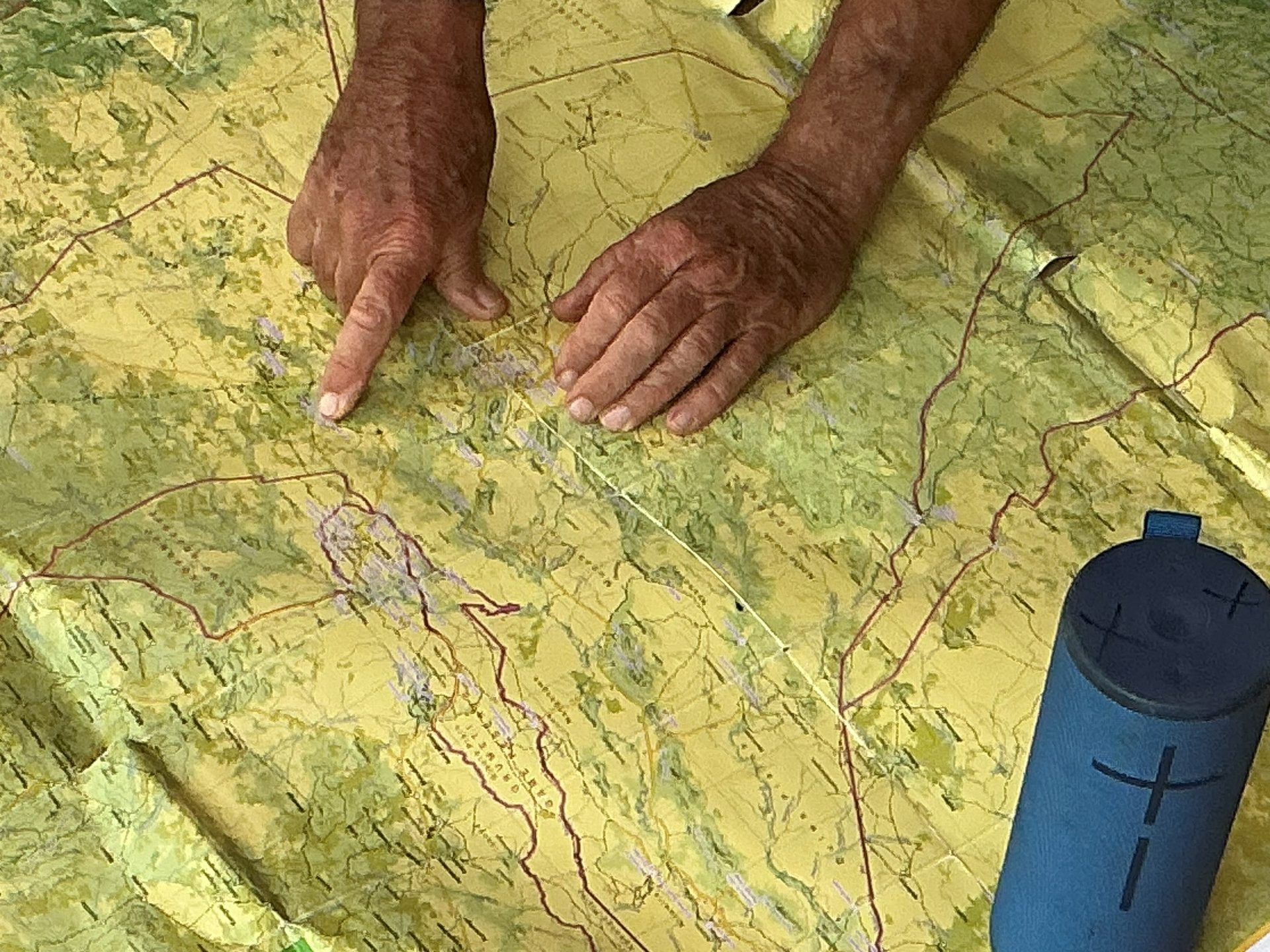 Close-up of a guide's hands on the Serengeti topographic map — pointing to a specific location, the conservation area route marked in red