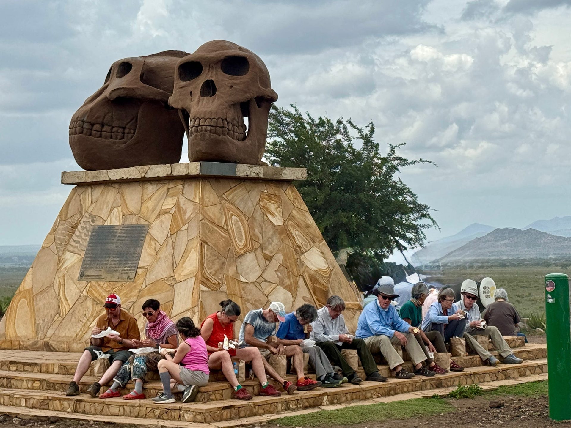 The whole group eating lunch at the base of the Olduvai Gorge skull monument