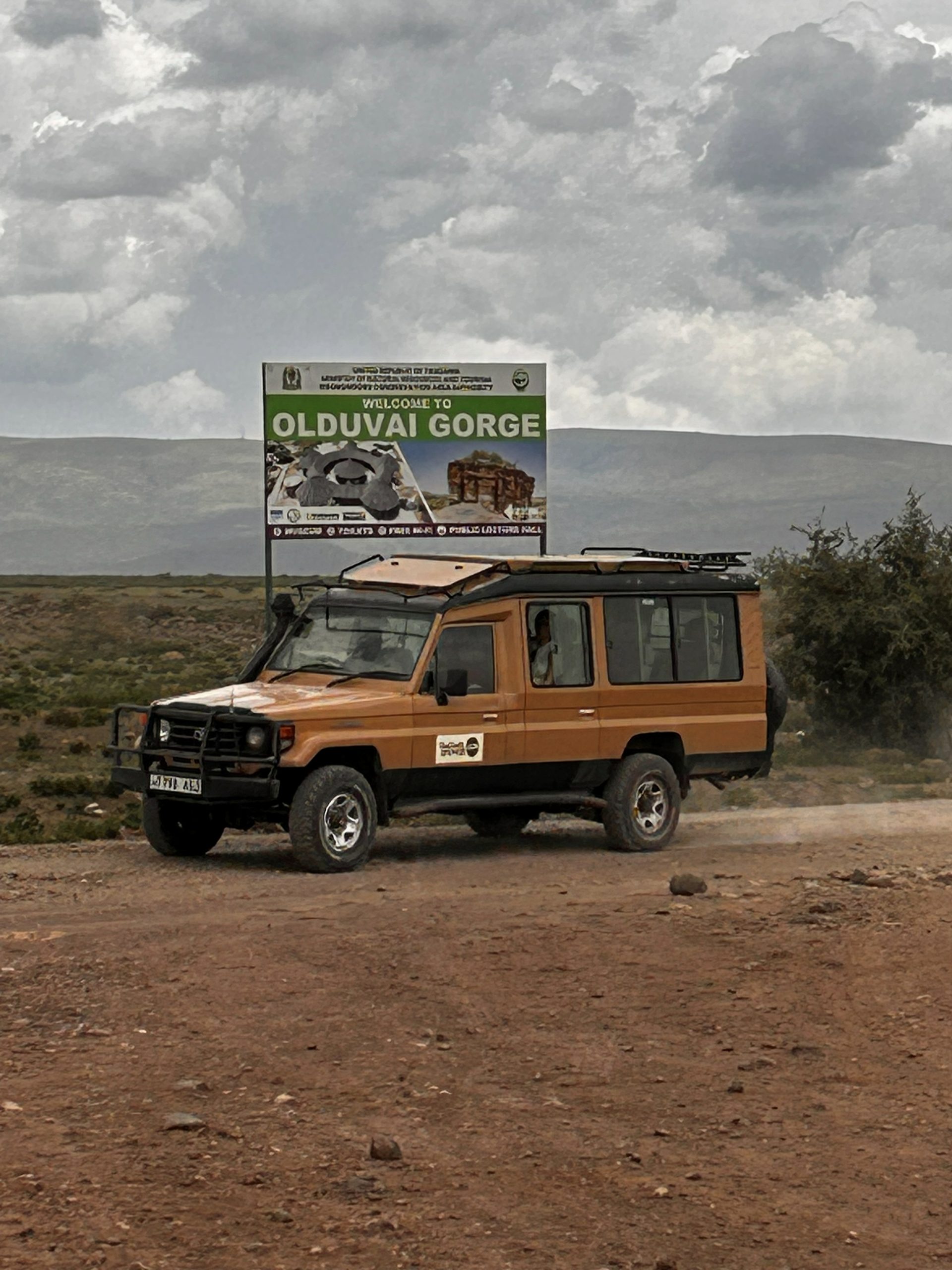 Thomson Land Cruiser at the Welcome to Olduvai Gorge sign — the crater highlands rising behind