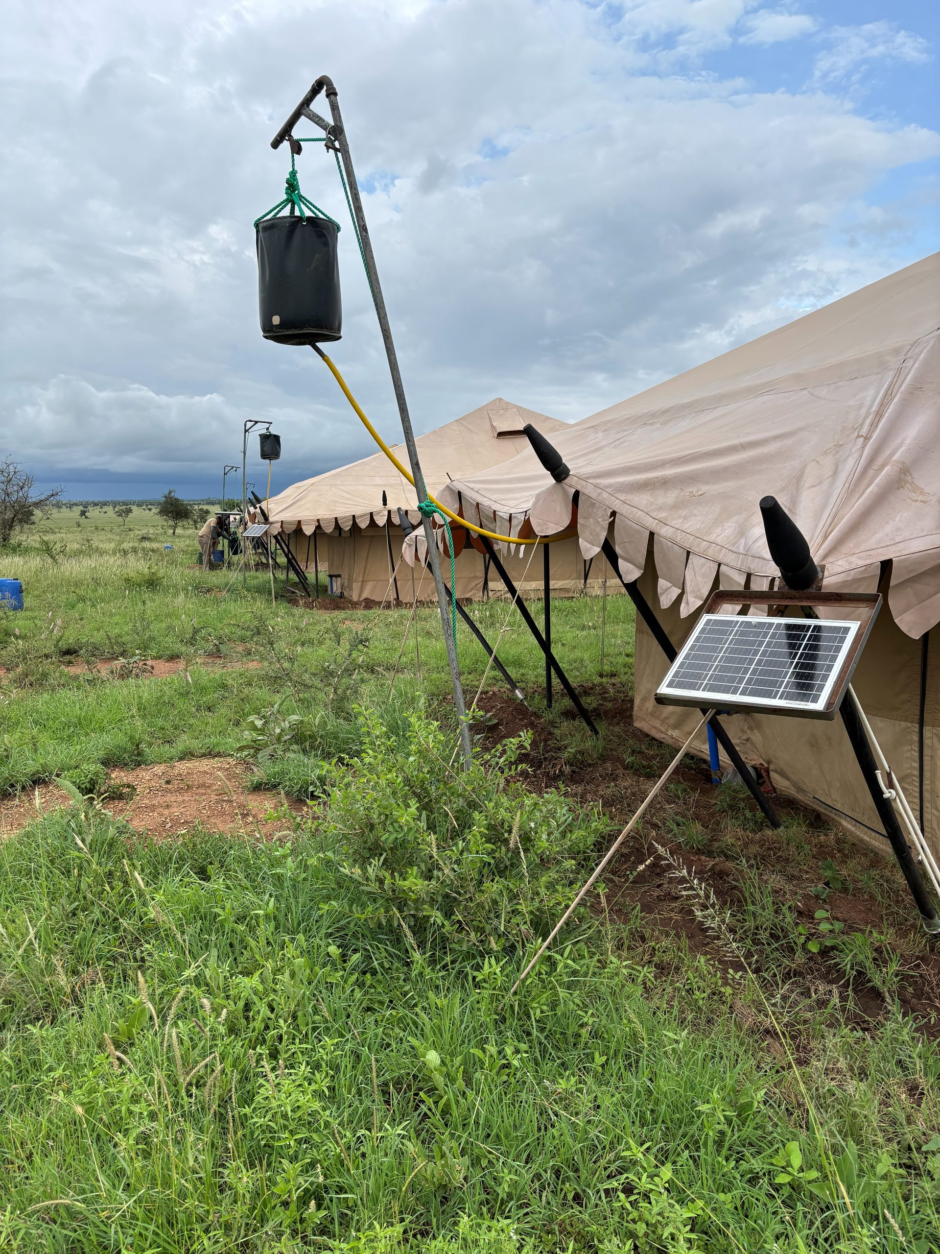 The Nyumba camp bucket shower — a black canvas bucket hoisted on a pole beside the tent, a small solar panel on the guy-wire for charging